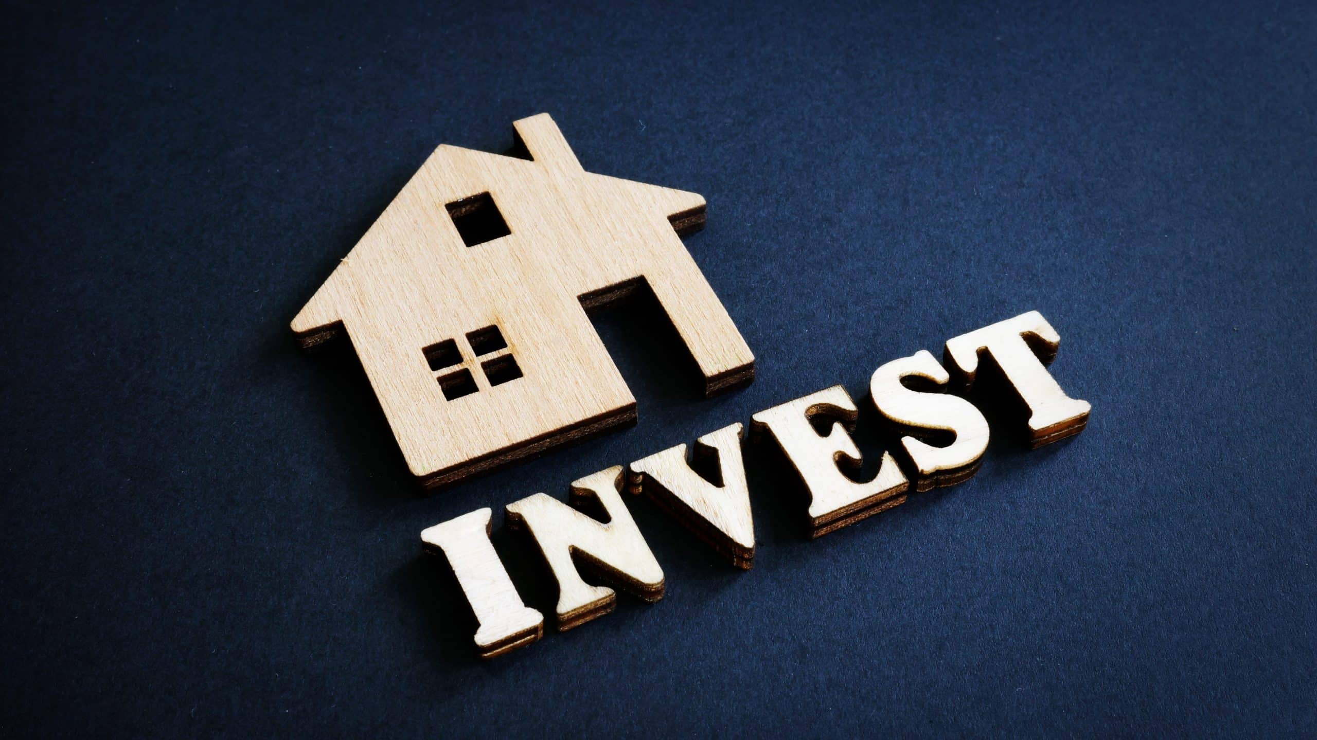 Word Invest and model of home from wood. Real Estate Investment concept.